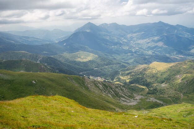 Paisaje de colinas cubiertas de vegetación con montañas rocosas bajo un cielo nublado