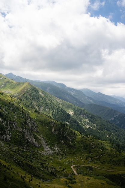 Paisaje de colinas cubiertas de vegetación con montañas rocosas bajo un cielo nublado