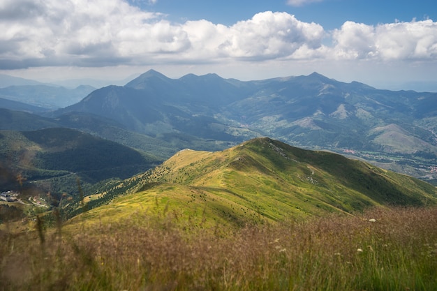 Paisaje de colinas cubiertas de vegetación con montañas rocosas bajo un cielo nublado en el