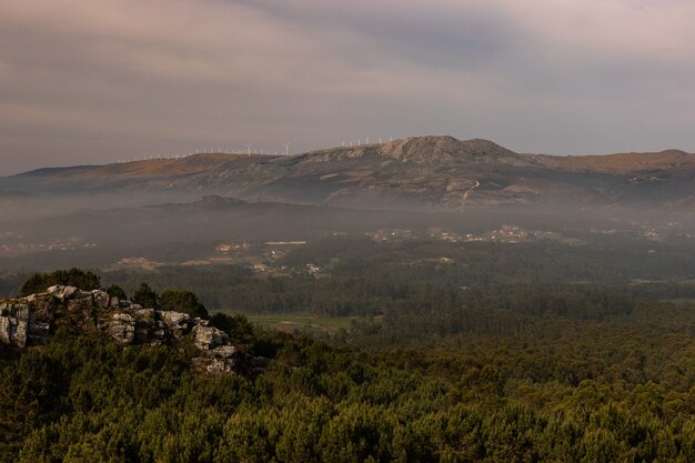 Paisaje de colinas y rocas cubiertas de vegetación y niebla bajo un cielo nublado en la noche