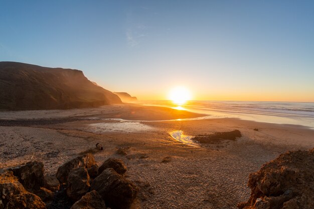 Paisaje de una costa rodeada de montañas y mar bajo un cielo azul durante el atardecer