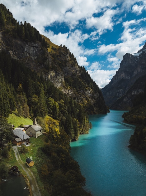 Paisaje de un hermoso río entre las montañas y pequeñas casas bajo el cielo nublado.