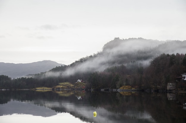 Paisaje de un lago rodeado de montañas cubiertas de bosques y niebla que se refleja en el agua