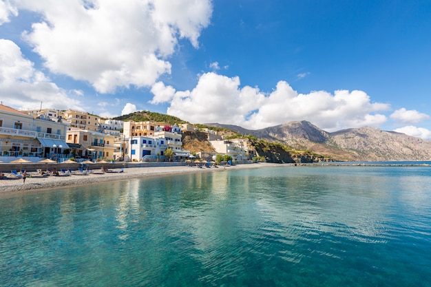 Foto gratuita paisaje de un mar rodeado de montañas, edificios y playas bajo un cielo azul nublado en grecia