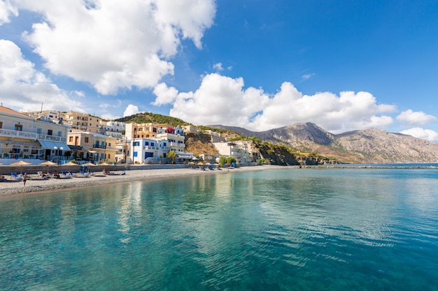Paisaje de un mar rodeado de montañas, edificios y playas bajo un cielo azul nublado en Grecia