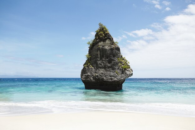 Paisaje marino ideal y tranquilo: cielo azul, isla de piedra con vegetación en medio del océano con agua turquesa.