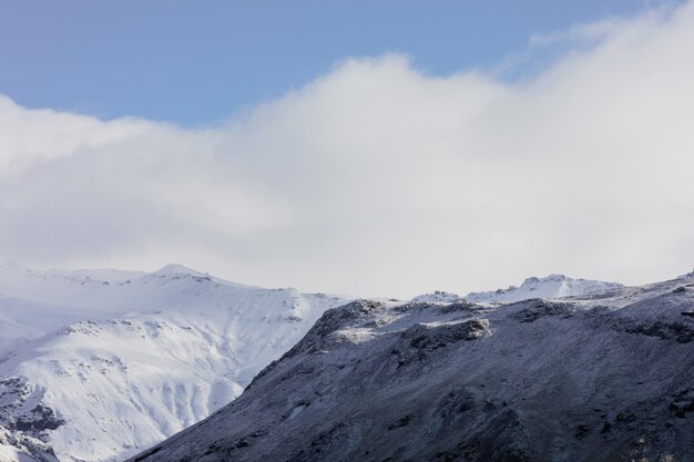 Paisaje de montañas cubiertas de nieve bajo un cielo nublado azul en Islandia