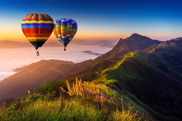 Paisaje de niebla matutina y montañas con globos aerostáticos al amanecer.