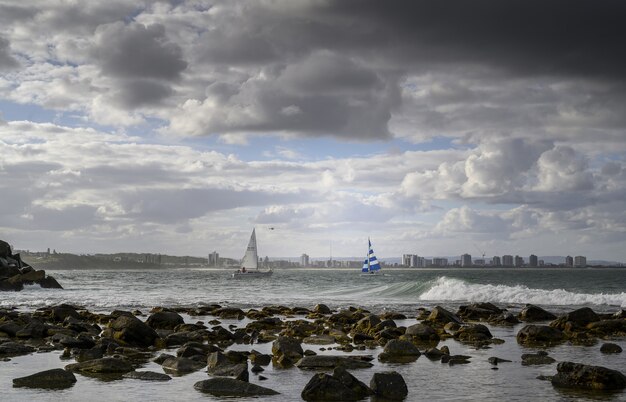 Paisaje de la orilla rodeada por el mar con barcos y surfistas bajo un cielo nublado