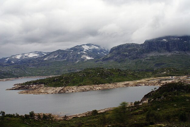 Paisaje de un paisaje con un lago rodeado de verdes montañas bajo un cielo nublado en Noruega