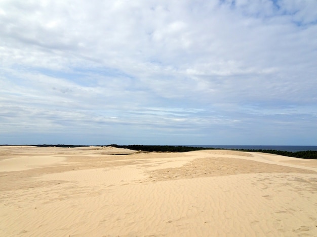 Paisaje de playa de arena bajo un cielo nublado azul en Leba, Polonia