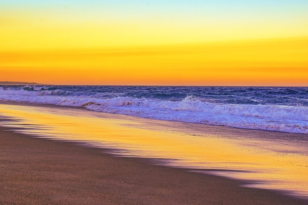Foto gratuita paisaje de una playa rodeada de olas del mar durante una puesta de sol naranja en la noche