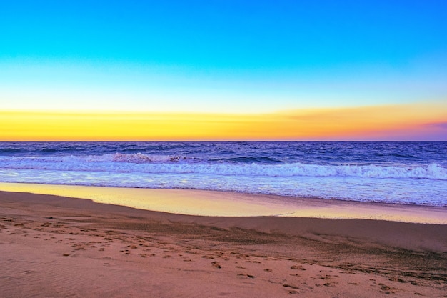 Paisaje de una playa rodeada de olas del mar durante una puesta de sol naranja en la noche