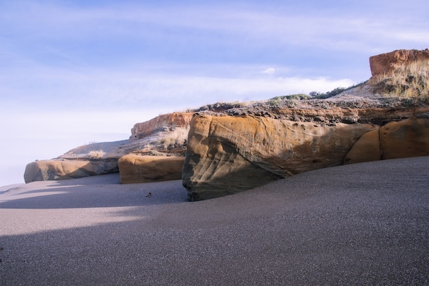 Paisaje de la playa rodeada de rocas bajo la luz del sol y un cielo nublado durante el día