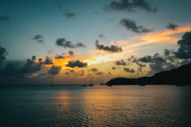 Paisaje de puesta de sol con una silueta de montaña y barcos en el mar