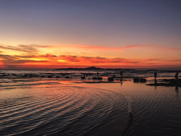Paisaje de puesta de sol con una silueta de personas en la playa.
