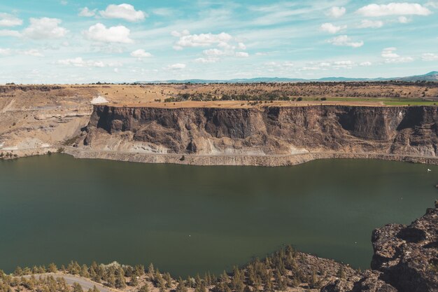 Paisaje de un río rodeado de acantilados cubiertos de vegetación bajo un cielo azul y la luz del sol