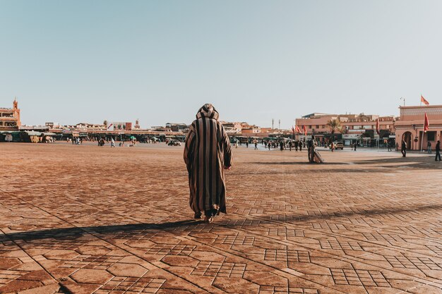 Paisaje soleado de un hombre árabe en thawb despojado caminando en la gran zona urbana