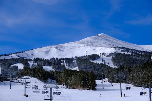 Paisaje de teleféricos rodeado de colinas y bosques cubiertos de nieve bajo un cielo azul