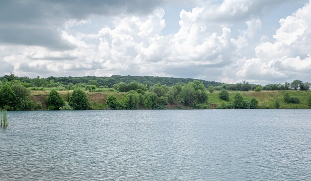 Paisaje de verano en el campo con río, bosque y nubes.