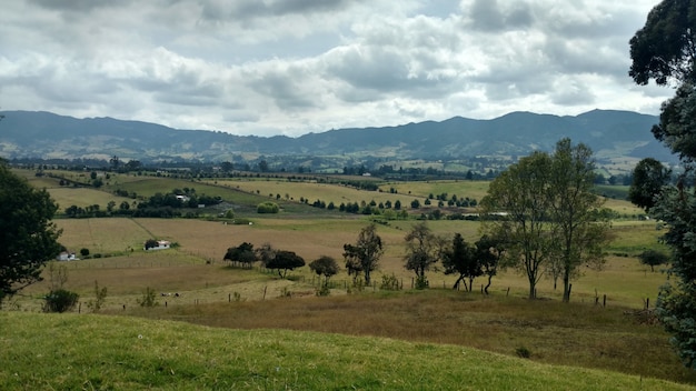 Paisaje de una zona rural rodeada de colinas cubiertas de vegetación bajo un cielo nublado durante el día