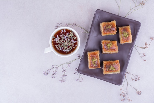 Pakhlava turco en bandeja de cerámica negra con una taza de té de hierbas.