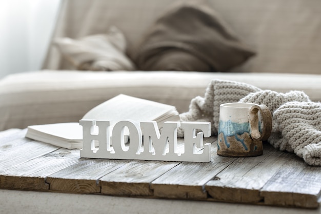 Palabra decorativa hogar, taza, libro y elemento de punto en el interior de la habitación.