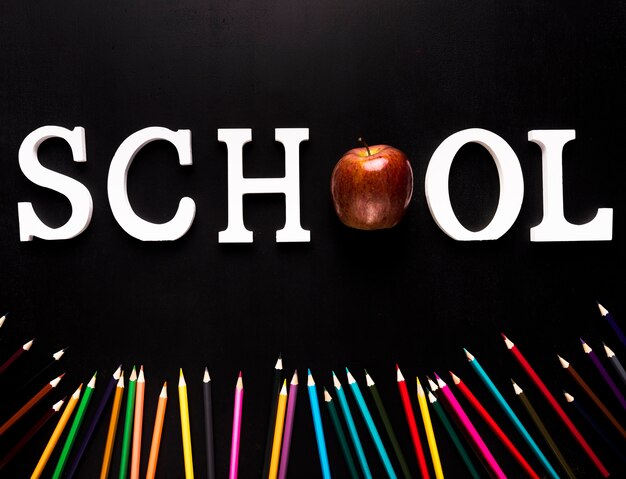 Palabra de la escuela y lápices de colores esparcidos sobre fondo negro