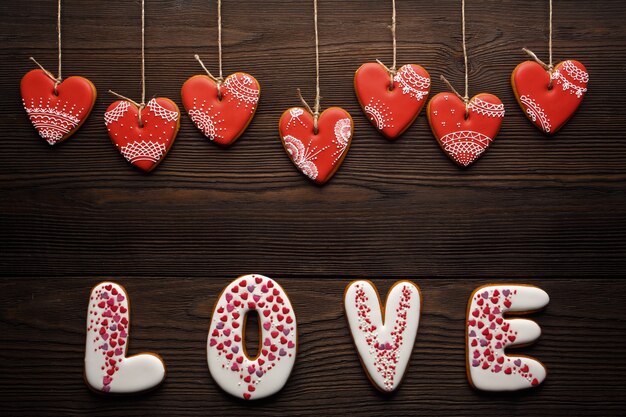 Palabra "love" hecha de galletas con galletas con forma de corazón colgando de cuerdas sobre una mesa de madera