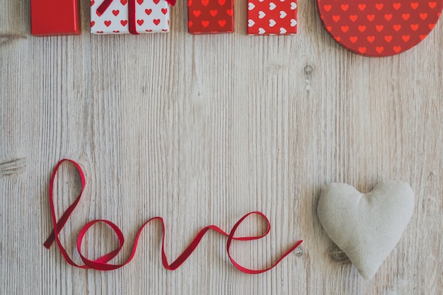 Palabra "love" con regalos arriba y un corazón blanco de tela a su lado