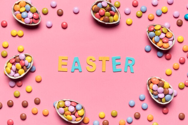 Palabra de Pascua rodeada de caramelos de gemas de colores y huevos de Pascua sobre fondo rosa