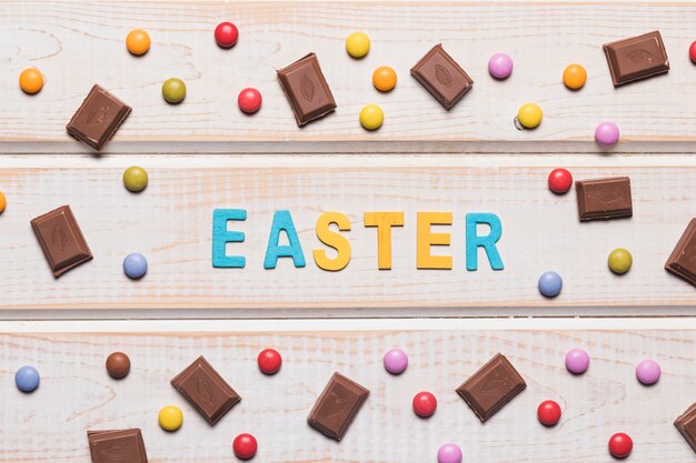 Palabra de Pascua rodeada con gemas multicolores y trozos de chocolate en mesa de madera