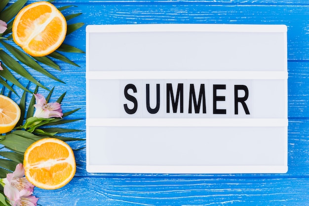 Palabra del verano en la tableta cerca de las hojas de la planta con naranjas frescas