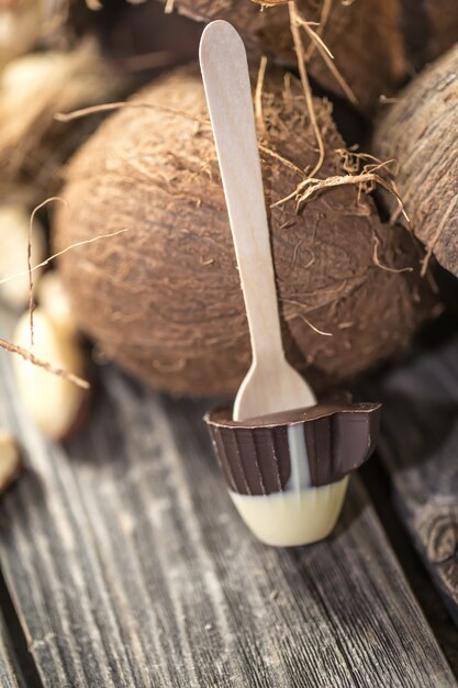 Paleta de chocolate en forma de pequeña taza con coco y nueces sobre madera