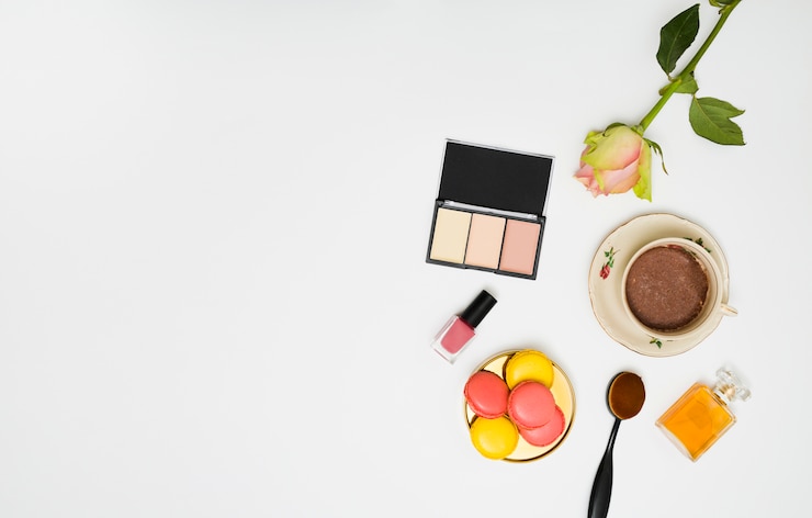 Foto gratuito paleta compacta de polvos faciales; rosa; botella de esmalte de uñas; pincel de maquillaje ovalado; botella de perfume y café sobre fondo blanco