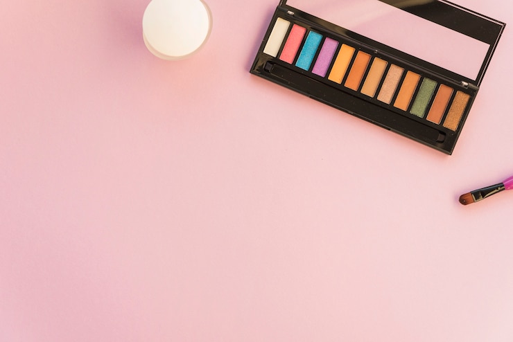 Foto gratuito paleta de maquillaje con pincel sobre fondo coloreado.