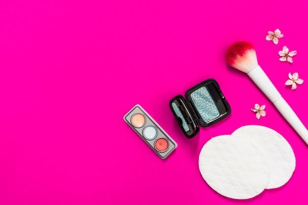 Paleta de sombra de ojos; brocha de maquillaje; Almohadillas de algodón y flor sobre fondo rosa