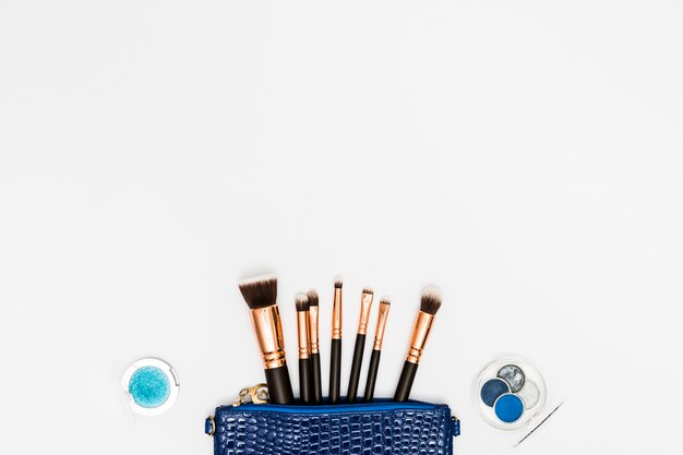 Paleta de sombras de ojos con pinceles de maquillaje de una bolsa azul sobre fondo blanco