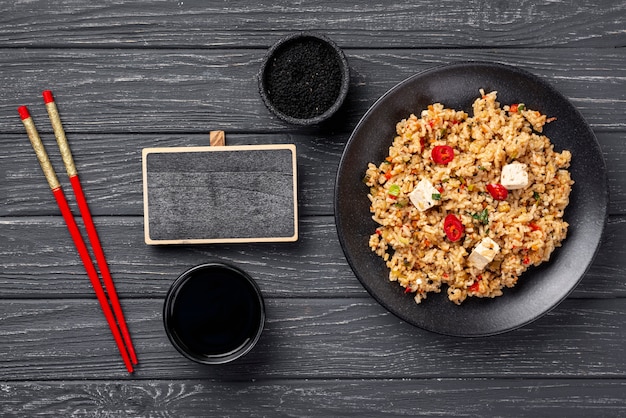 Palillos de alto ángulo y arroz con verduras en un plato con pizarra en blanco