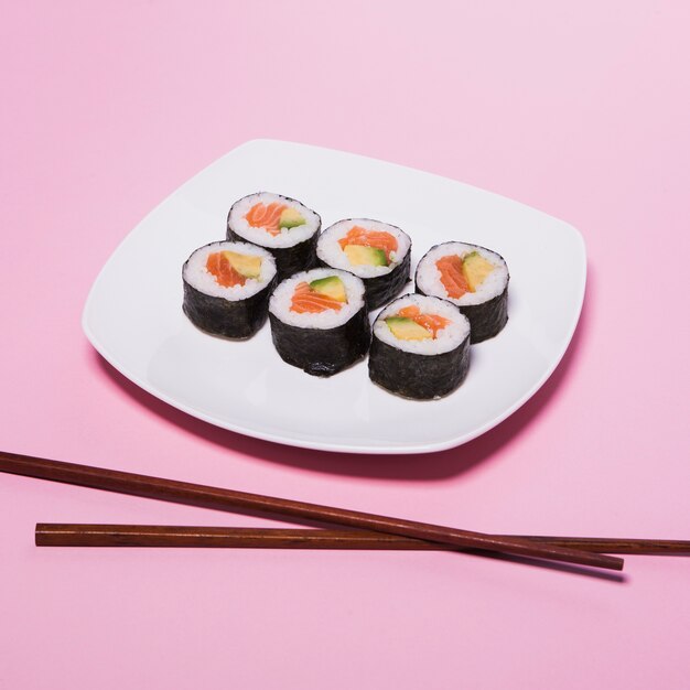 Palillos cerca de la placa con sushi en rosa