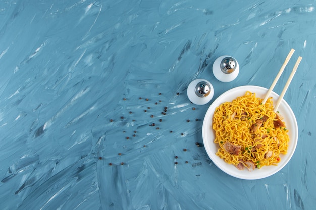 Palillos con fideos de carne en un plato, sobre el fondo de mármol.