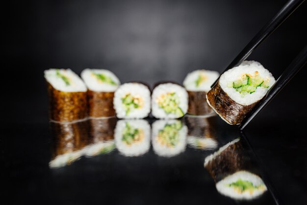 Palillos que sostienen el rodillo hecho de Nori, arroz adobado, blanco de sésamo, pepino.