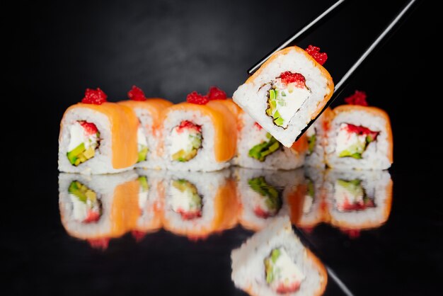 Palillos con rollo de sushi Filadelfia con fondo negro hecho de salmón