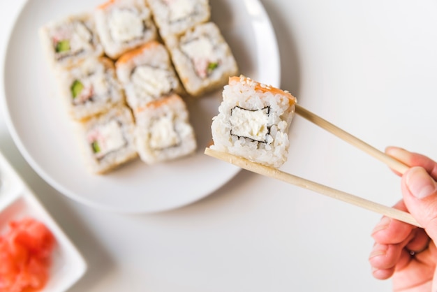 Palillos sosteniendo un rollo de sushi
