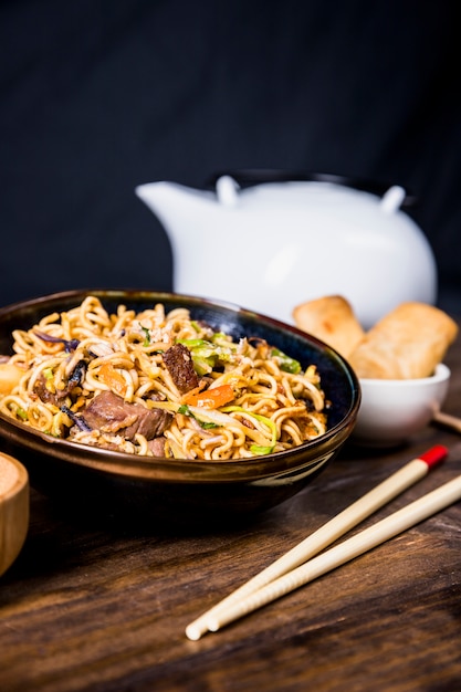 Palillos y tazón de fideos deliciosos con carne de res en el escritorio de madera