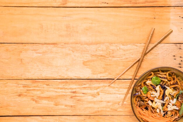 Los palillos y el tazón de fideos udon adornan con camarones; nueces; hierbas y camarones sobre la mesa