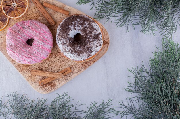 Palitos de canela aromáticos, rosquillas y rodajas de naranja secas sobre una placa sobre fondo blanco.