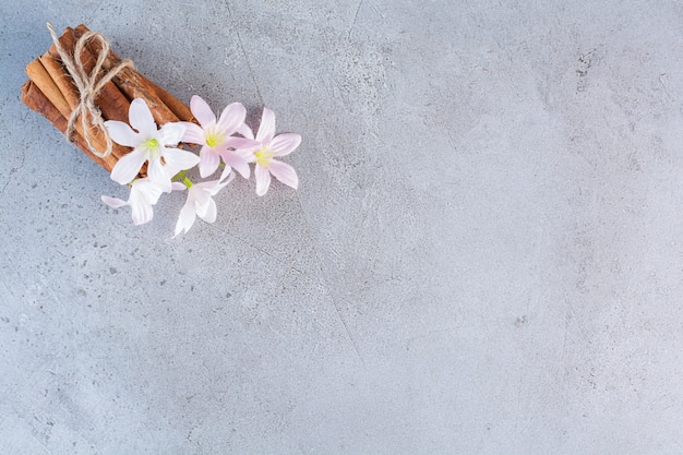 Palitos de canela en cuerda con flores blancas y rosadas sobre fondo gris.