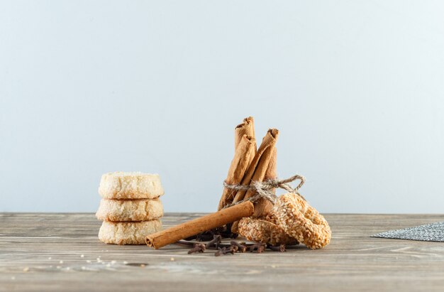 Palitos de canela con galletas, clavo, mantel individual en la pared de madera y blanca, vista lateral.