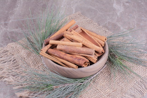 Palitos de canela en una taza de madera con rama de roble alrededor